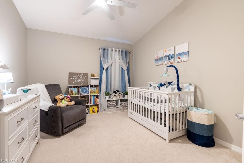 Bedroom with a nursery area, light carpet, a ceiling fan, and vaulted ceiling