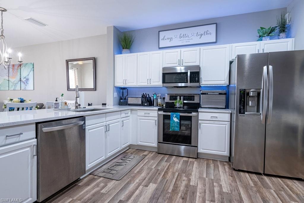 Kitchen featuring appliances with stainless steel finishes, white cabinets, light wood-style floors, pendant lighting, and light stone countertops