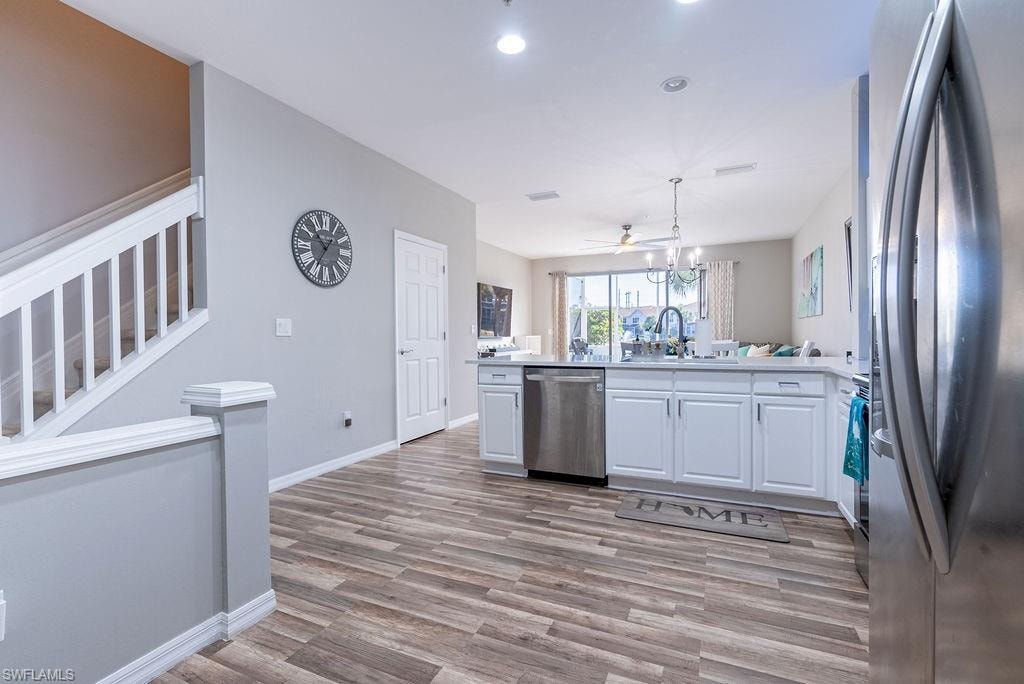 Kitchen featuring appliances with stainless steel finishes, white cabinets, a peninsula, hanging light fixtures, and light wood-style floors