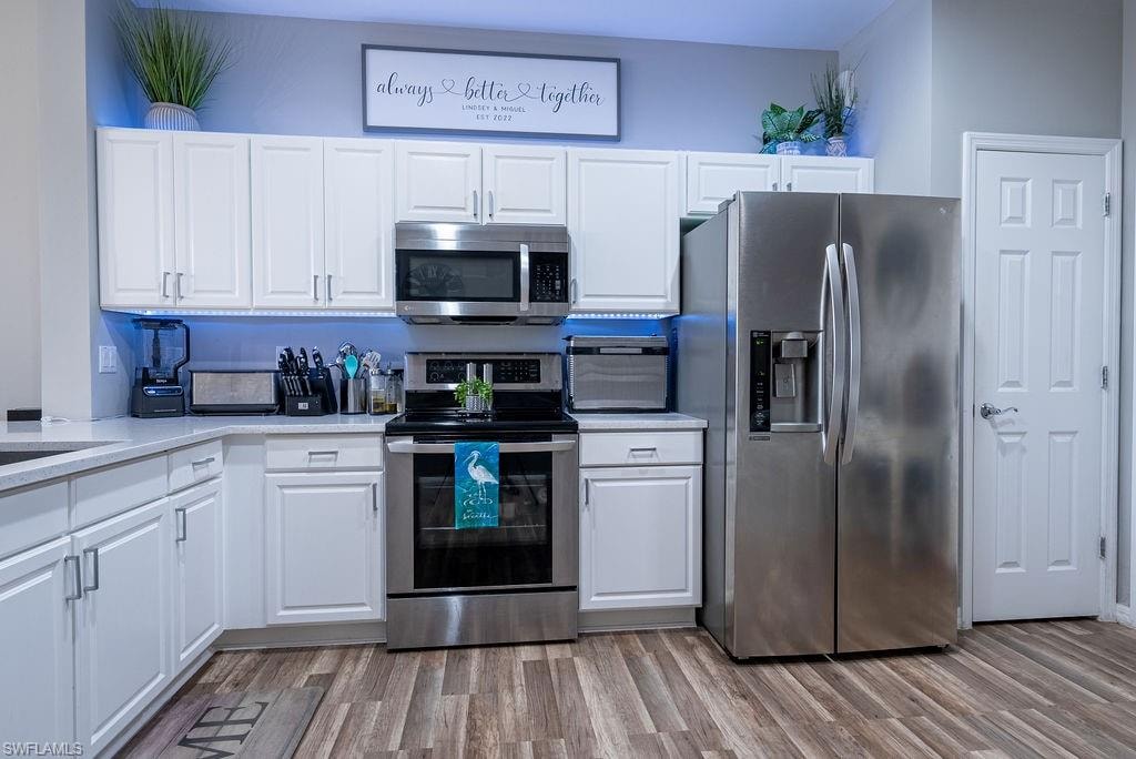Kitchen with appliances with stainless steel finishes, white cabinets, light wood-style flooring, and light stone countertops