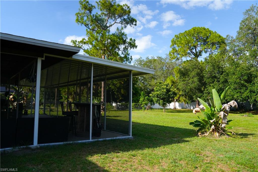 Screened lanai with concrete patio and built-in bar, overlooking a spacious lawn with mature trees and established landscaping