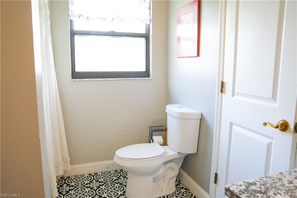 Bathroom featuring patterned tile flooring, a white toilet, and a window with a granite-look sill