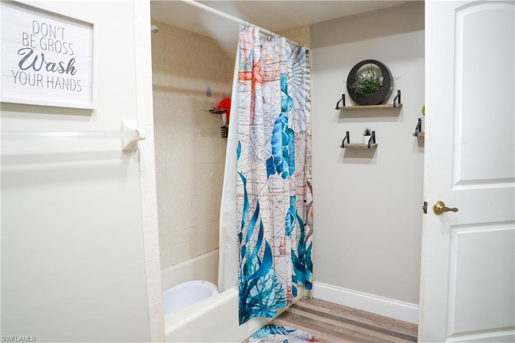 Bathroom featuring a white tub with tiled surround, wood-finish flooring, and wall-mounted shelving