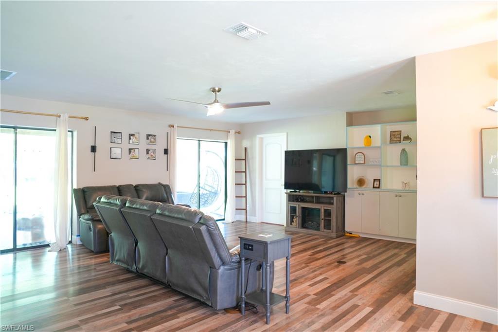 Spacious living area featuring wood-finish flooring, a ceiling fan, and built-in cabinetry with shelving