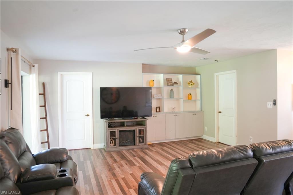 Living area featuring wood-finish flooring, a contemporary ceiling fan, built-in shelving, and light-toned walls
