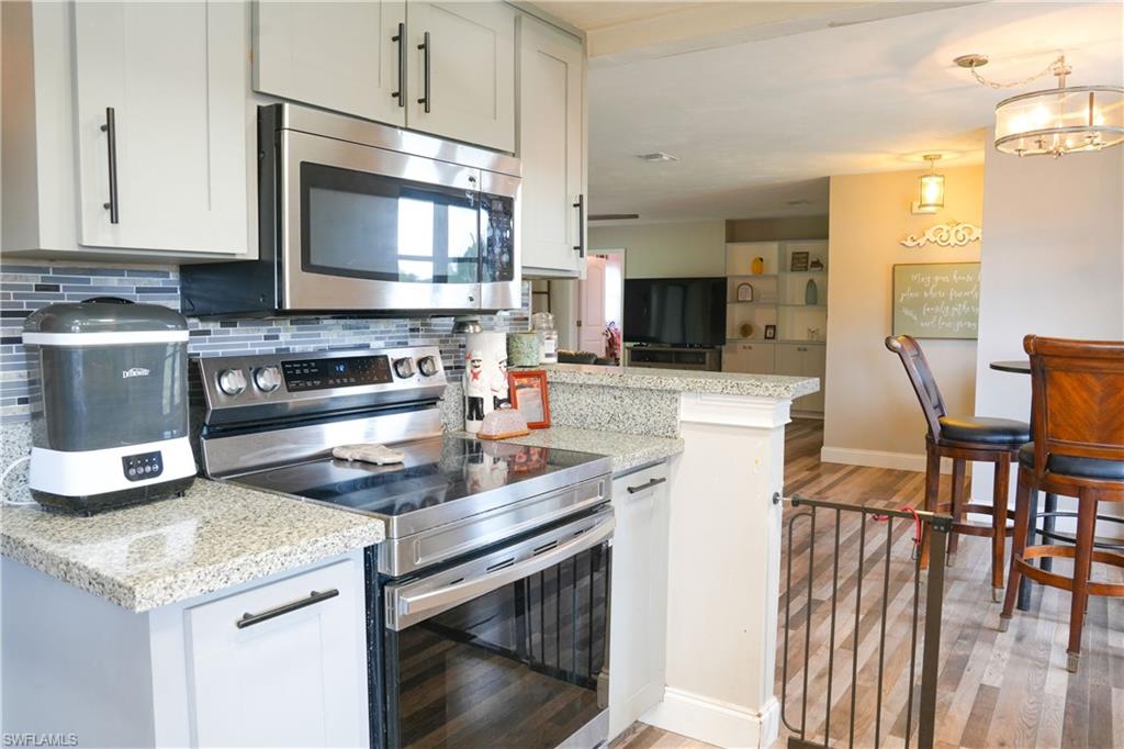 Modern kitchen featuring stainless steel appliances, light-toned cabinetry with dark hardware, a tile backsplash, and granite countertops