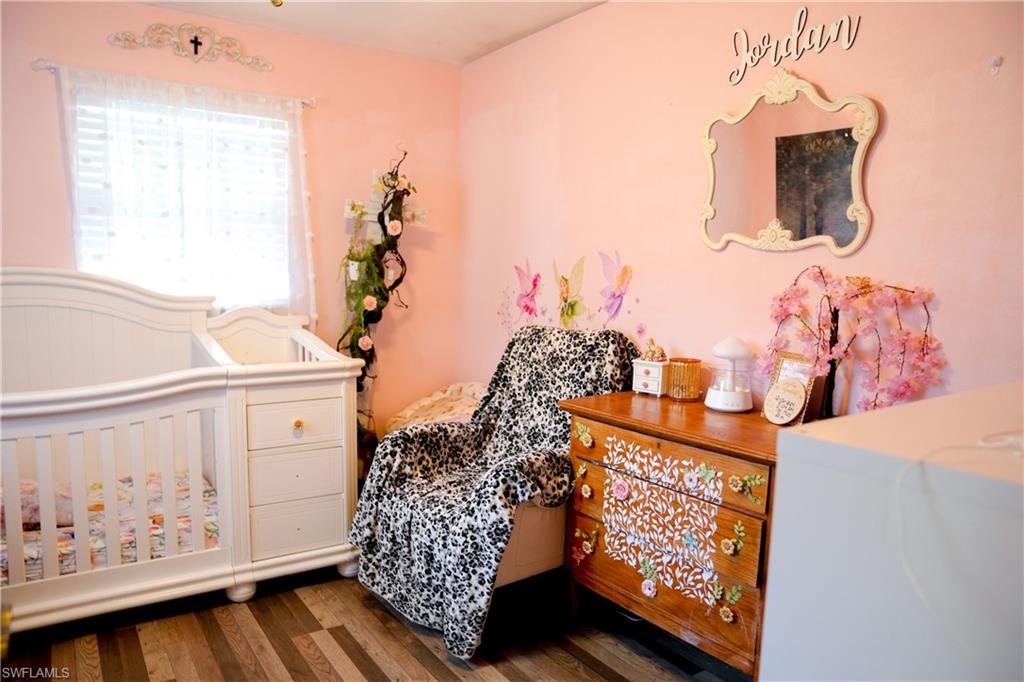 Room featuring wood-finish flooring, light pink walls, and a white framed window with sheer curtains