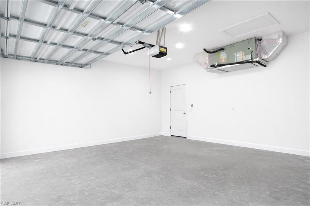 Spacious garage with a concrete floor, bright white walls, and a recessed panel door