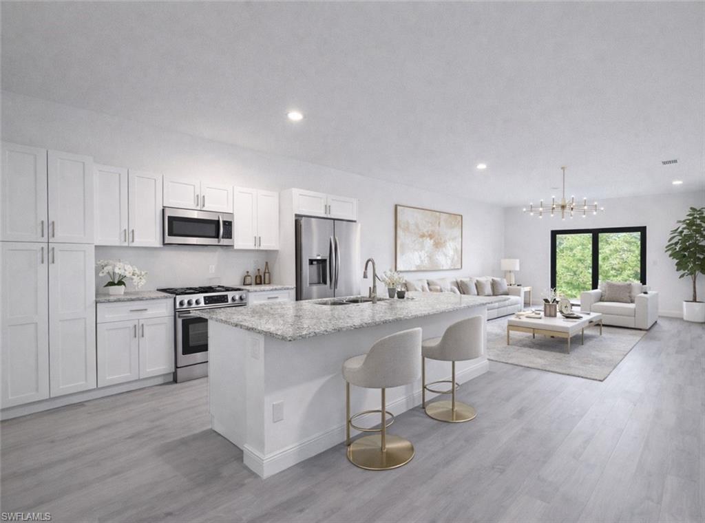 Open-concept living area featuring a kitchen with white cabinetry, stainless steel appliances, and a central island with a light-toned countertop