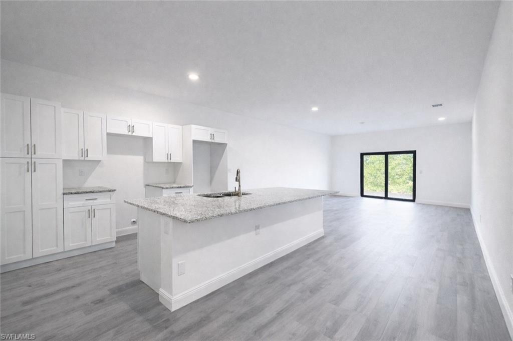 Open-concept kitchen and living area featuring white cabinetry, light-toned granite countertops, and a central island with a stainless steel sink
