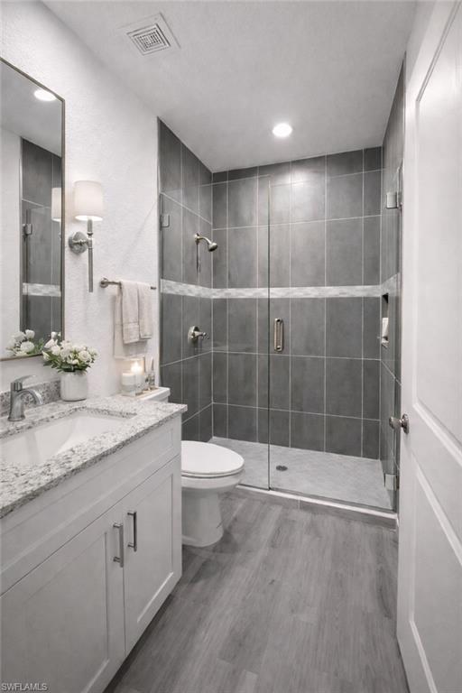 Bathroom featuring a frameless glass shower enclosure with dark gray subway tile, a white vanity with a granite countertop, and wood-finish flooring