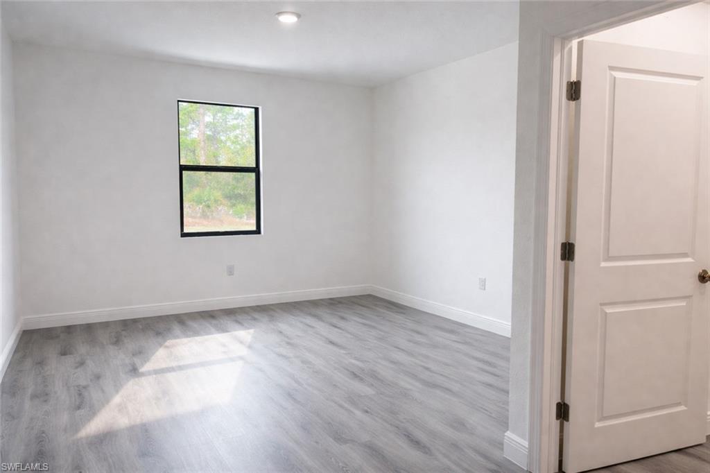 Spacious room featuring light wood-finish flooring, white baseboards, and a single recessed ceiling light