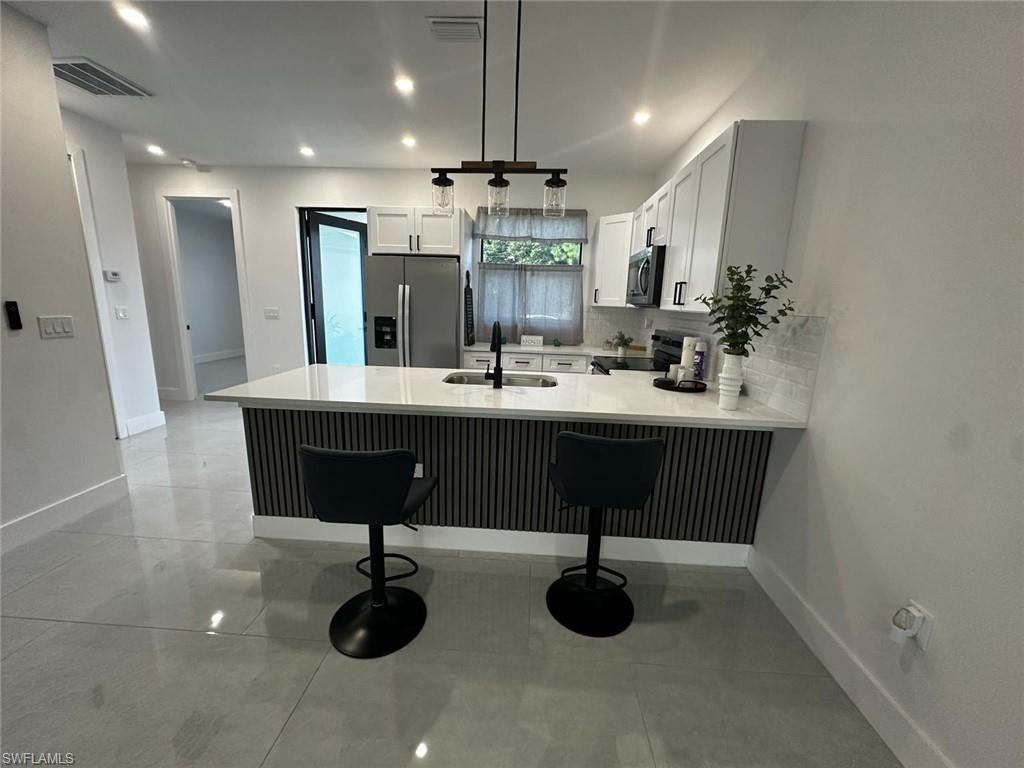 Modern kitchen featuring a waterfall island with slatted paneling, light-toned cabinetry, stainless steel refrigerator, contemporary pendant lighting, and light tile flooring