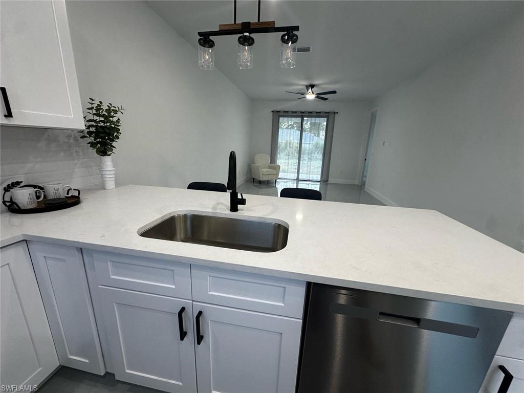Kitchen island featuring a stainless steel sink with a matte black faucet, light-toned countertop, and white shaker-style cabinetry with black hardware