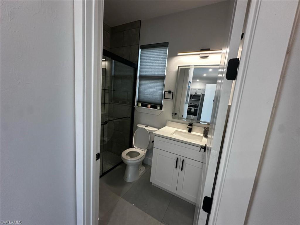 Contemporary bathroom featuring a frameless glass shower enclosure, a white vanity with double-door cabinetry, a rectangular undermount sink, a dark countertop, and a wall-mounted light fixture