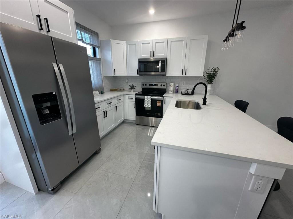 Modern kitchen featuring white shaker cabinetry, stainless steel appliances, a white subway tile backsplash, and light-toned tile flooring