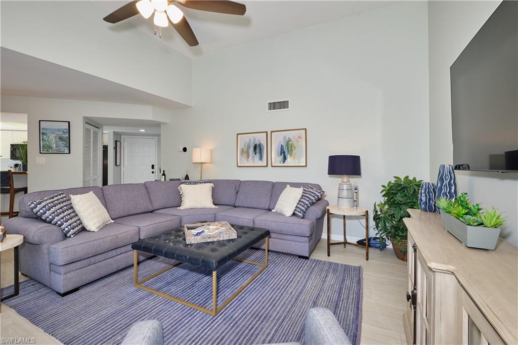 Living area featuring light wood finished floors, visible vents, ceiling fan, high vaulted ceiling, and baseboards
