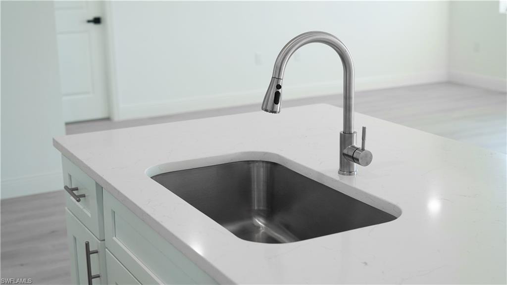 Kitchen island featuring a stainless steel undermount sink, gooseneck faucet with a pull-down sprayer, white countertop, and light-toned cabinetry with dark hardware