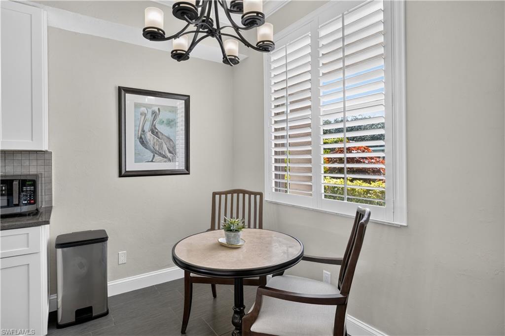 Breakfast nook featuring a large window with white plantation shutters, dark gray tile flooring, and a contemporary chandelier