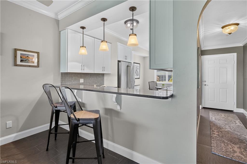 Kitchen peninsula featuring a dark countertop, three pendant light fixtures, and white shaker-style cabinetry