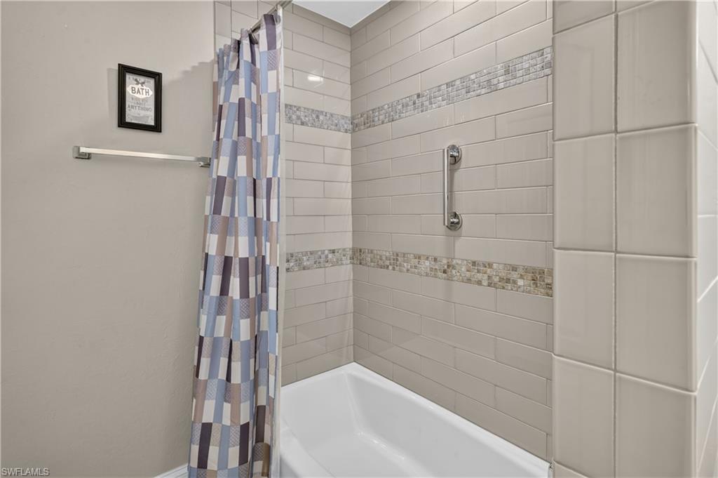White bathtub with subway tile surround, mosaic accent bands, and a chrome grab bar