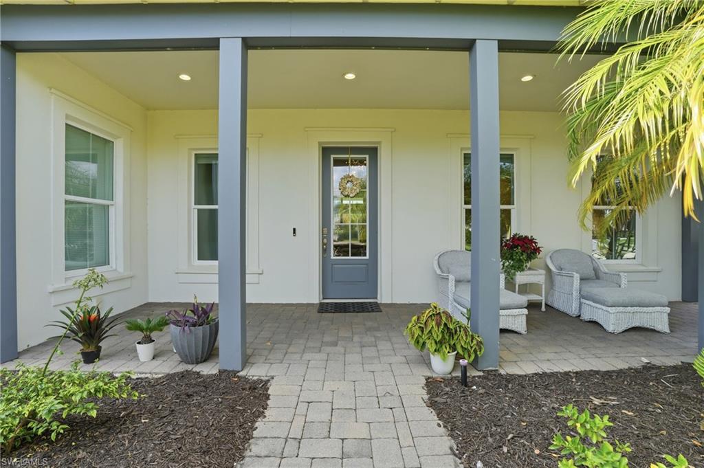 Covered front porch featuring a gray paneled door with glass inserts, white framed windows, recessed lighting, and a paved walkway
