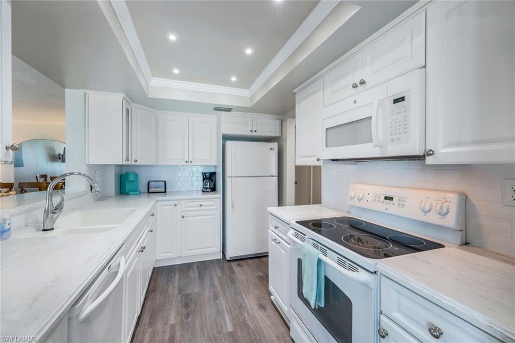 Kitchen featuring hardwood / wood-style flooring, a raised ceiling, white cabinetry, sink, and white appliances