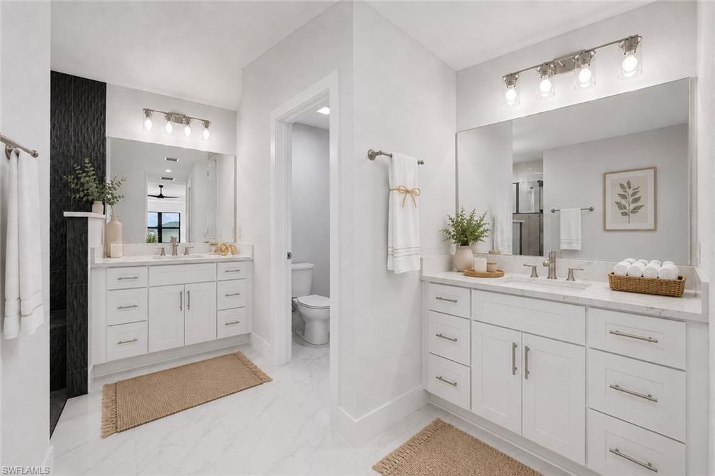 Dual vanity bathroom featuring white cabinetry with brushed nickel hardware, expansive mirrors, and white marble-finish countertops