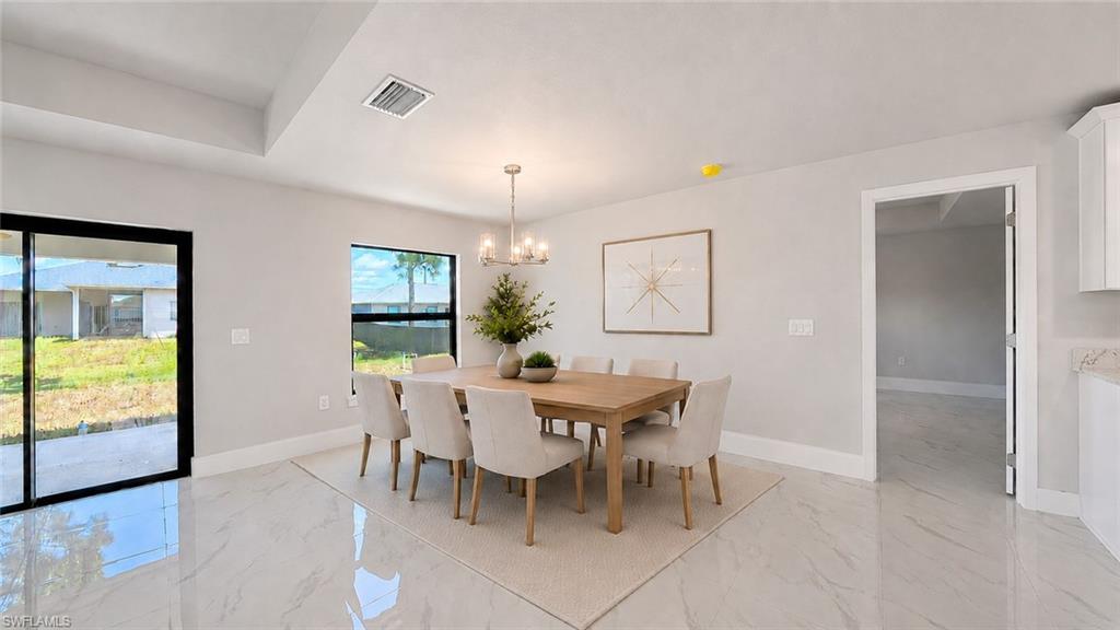 Bright, open dining area showcasing polished light stone flooring, a wood-finish dining table with upholstered chairs, and abundant natural light from expansive glass doors and windows