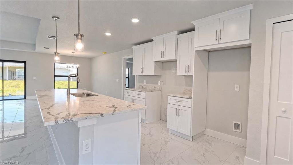 Open-concept kitchen featuring an expansive island with a waterfall-edge countertop, undermount sink, and pendant lighting