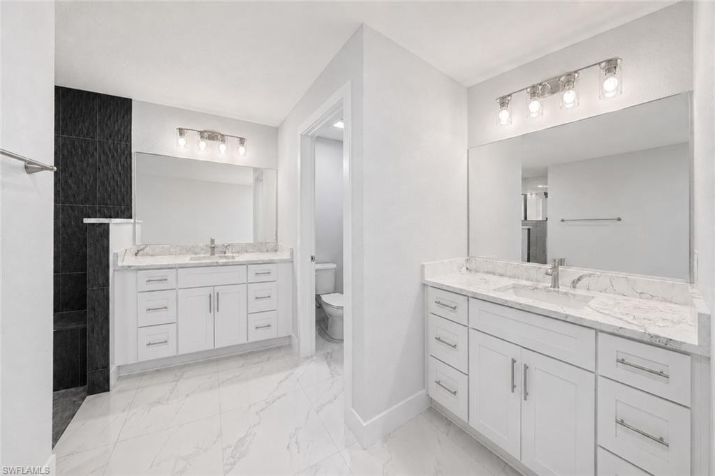 Dual vanity bathroom featuring white cabinetry, light-toned countertops, and large format floor tiling