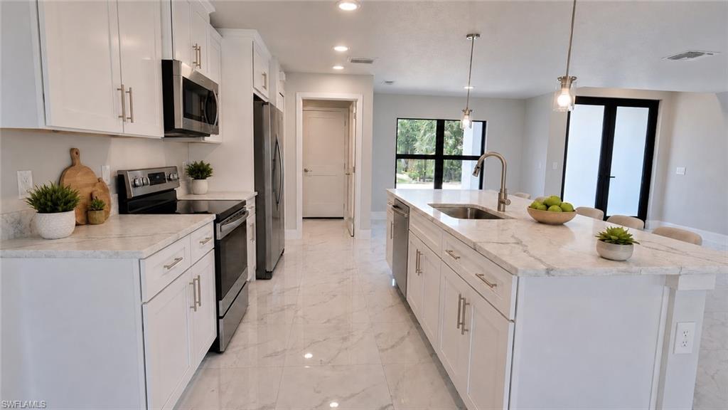Modern kitchen featuring white cabinetry with brushed nickel hardware, stainless steel appliances, quartz countertops, a large center island with pendant lighting, polished stone-finish flooring, and abundant natural light from multiple windows