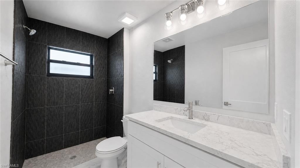 Contemporary bathroom featuring a spacious vanity with a white countertop and undermount sink, a large wall mirror, and a walk-in shower with dark textured tile walls and a window