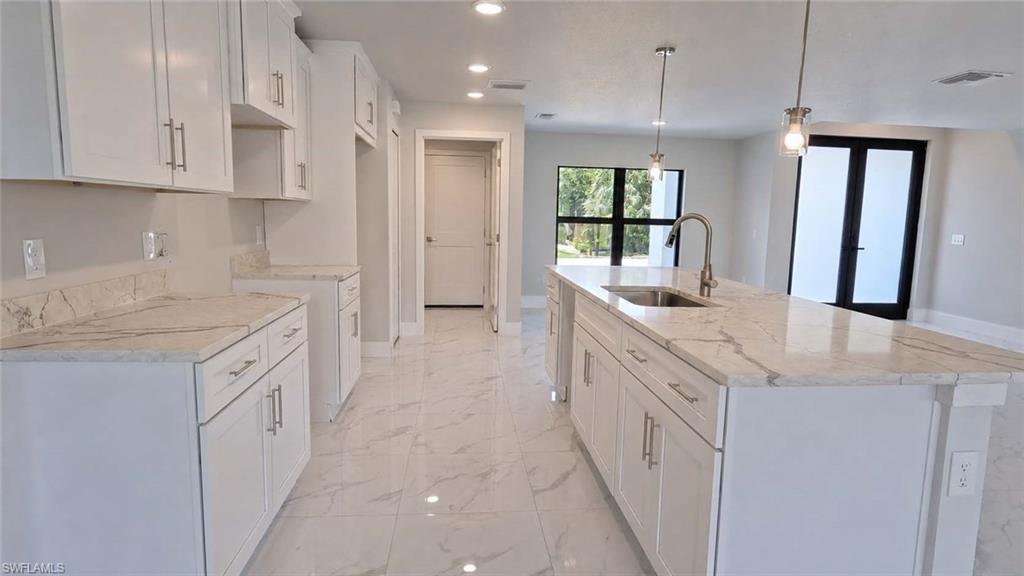 Spacious kitchen featuring an expansive center island with an undermount sink and gooseneck faucet, white shaker cabinetry with brushed nickel hardware, light-toned stone countertops, and large format marble-look tile flooring