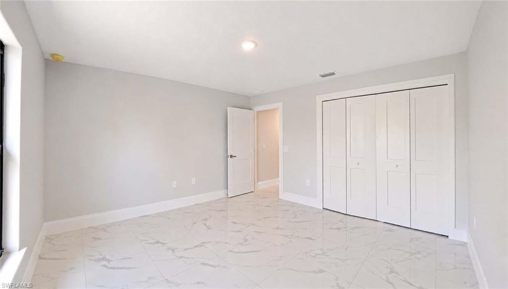 Spacious room featuring large format tile flooring, light gray wall color, white baseboards, and bi-fold closet doors