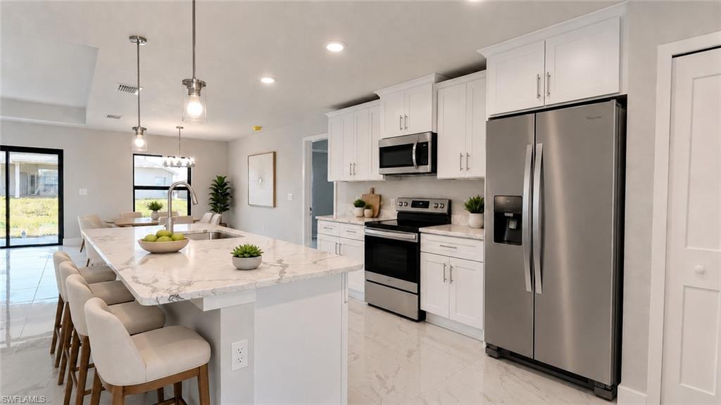 Spacious kitchen featuring an expansive island with a built-in sink, stainless steel appliances, white cabinetry, and recessed lighting