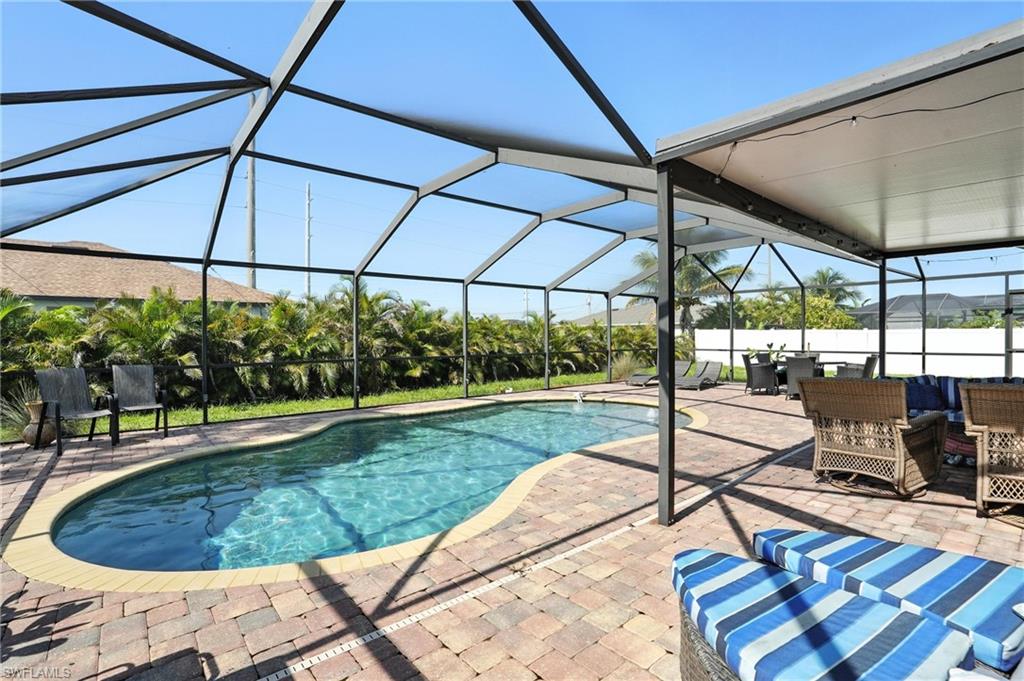 Screened pool enclosure featuring a free-form swimming pool with a paved deck, covered patio area, and perimeter landscaping