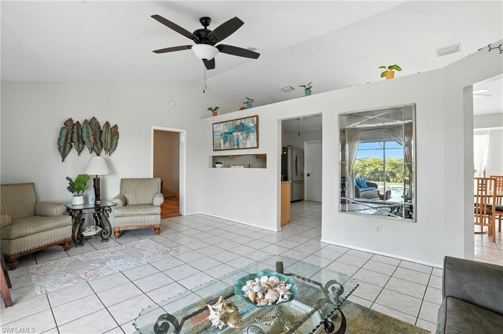 Vaulted ceiling living area featuring tile flooring, a dark-finish ceiling fan with integrated lighting, and a partial wall with an integrated decorative niche