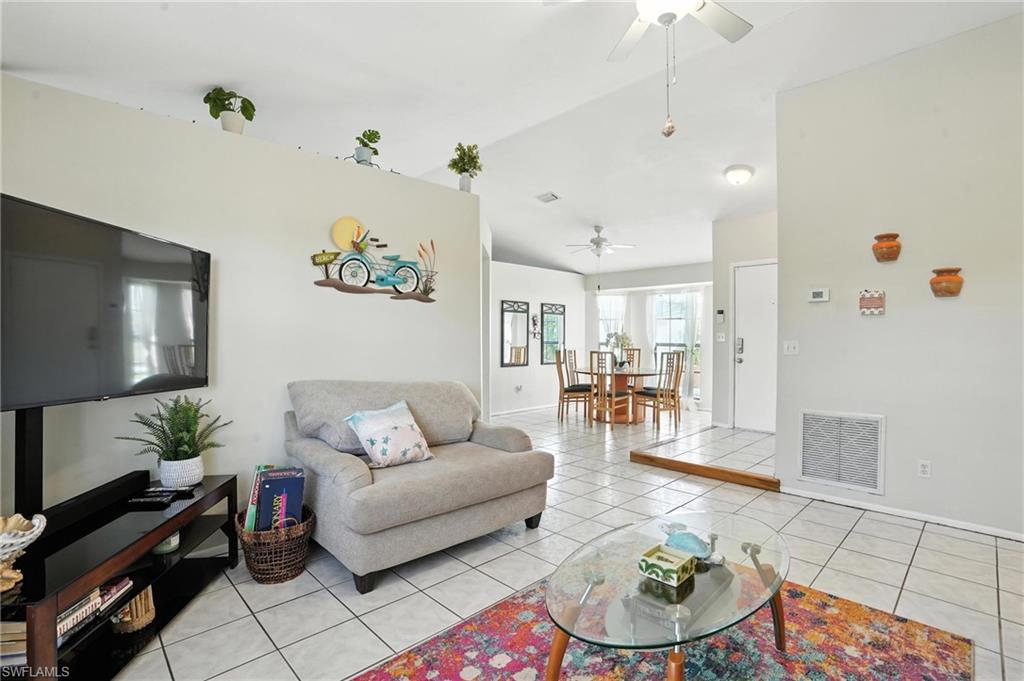 Spacious living area featuring neutral wall tones, square tile flooring, a vaulted ceiling with a ceiling fan, and a built-in architectural ledge