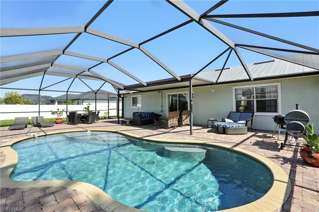 Screened-in outdoor living space featuring a freeform pool with integrated steps, brick paver decking, and a covered patio area with a metal roof