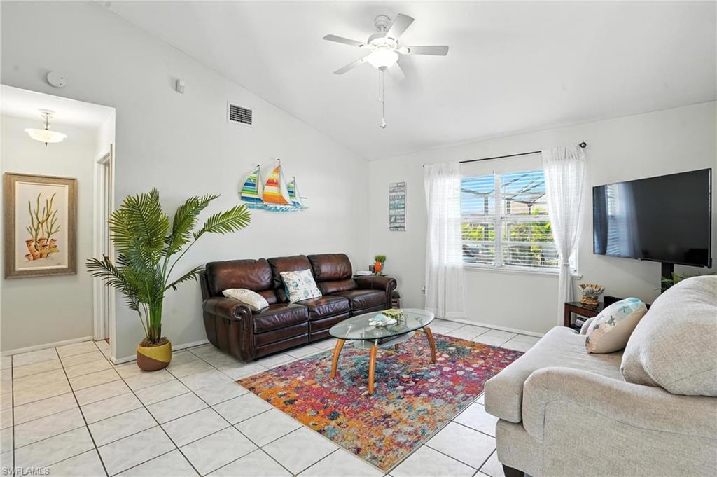 Living area featuring vaulted ceilings, white tile flooring, a ceiling fan with integrated lighting, and a prominent window with blinds