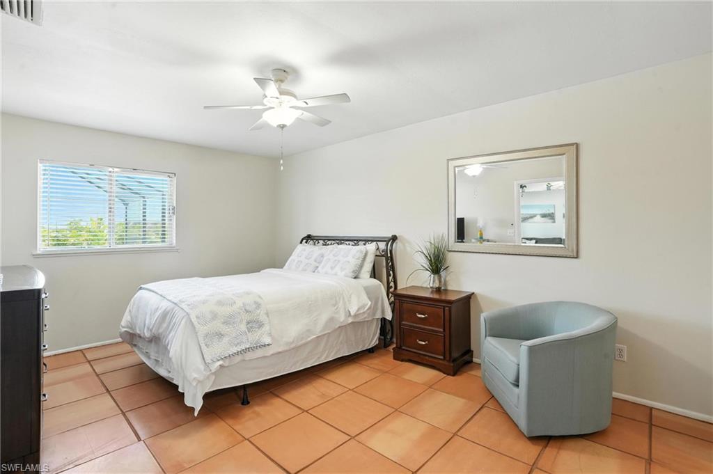 Spacious room featuring terra cotta tile flooring, a window with horizontal blinds, a ceiling fan with integrated lighting, and a wall-mounted mirror with a silver-toned frame