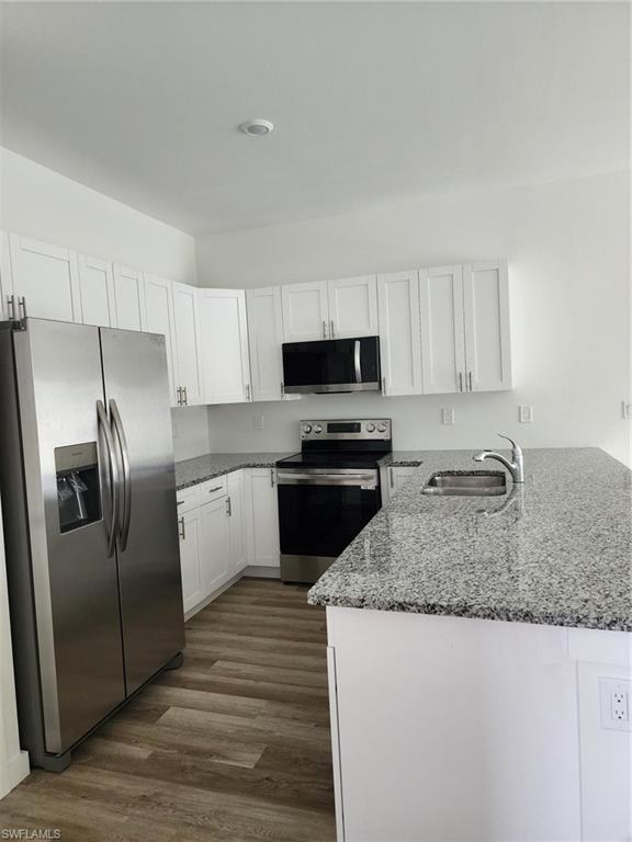 Kitchen featuring light stone countertops, stainless steel appliances, white cabinetry, and a peninsula