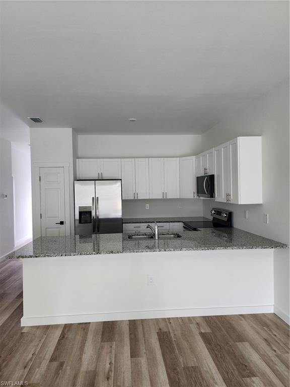 Kitchen featuring a peninsula, stainless steel appliances, white cabinetry, dark stone counters, and light wood finished floors