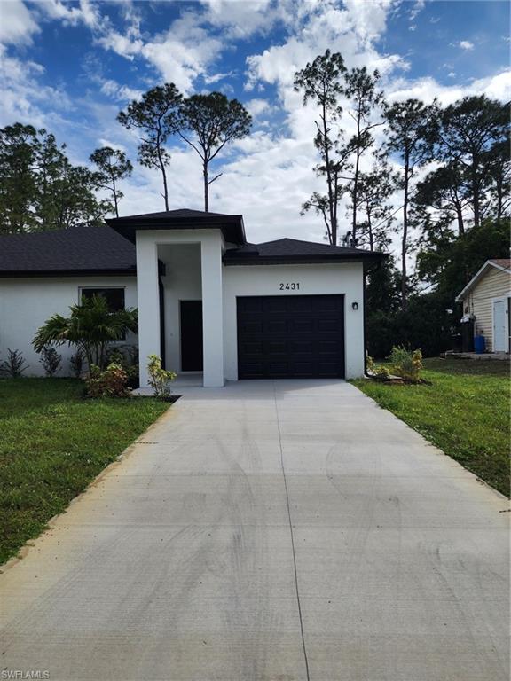 View of front facade featuring stucco siding, driveway, a front yard, and an attached garage