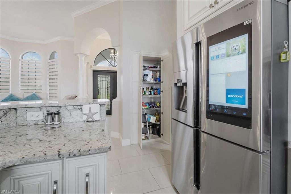 Kitchen featuring stainless steel fridge with ice dispenser, light stone counters, white cabinetry, light tile patterned floors, and crown molding