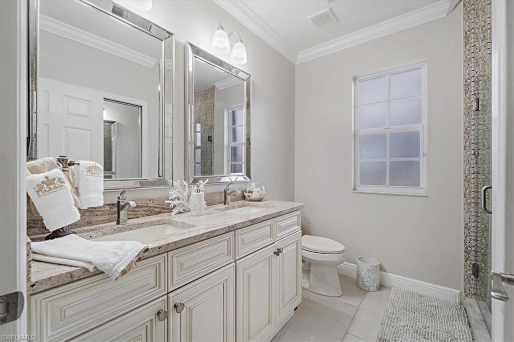 Bathroom featuring a shower stall, double vanity, light tile patterned floors, and crown molding
