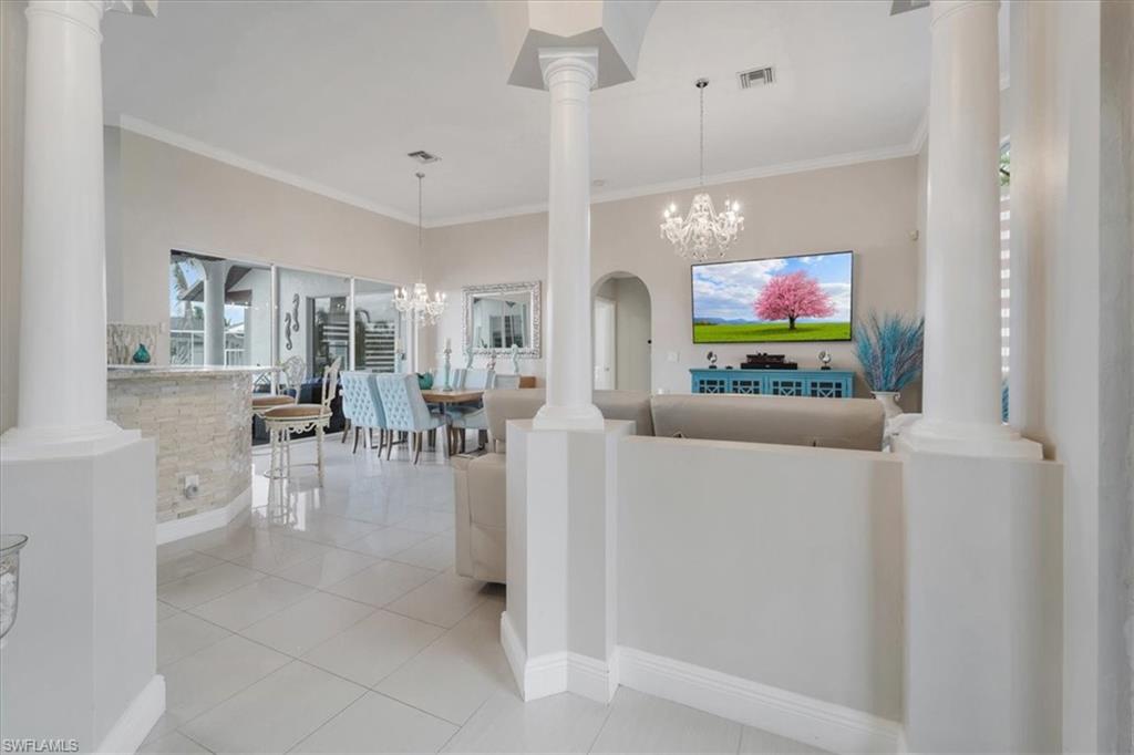 Living area featuring crown molding, ornate columns, a chandelier, and light tile patterned flooring