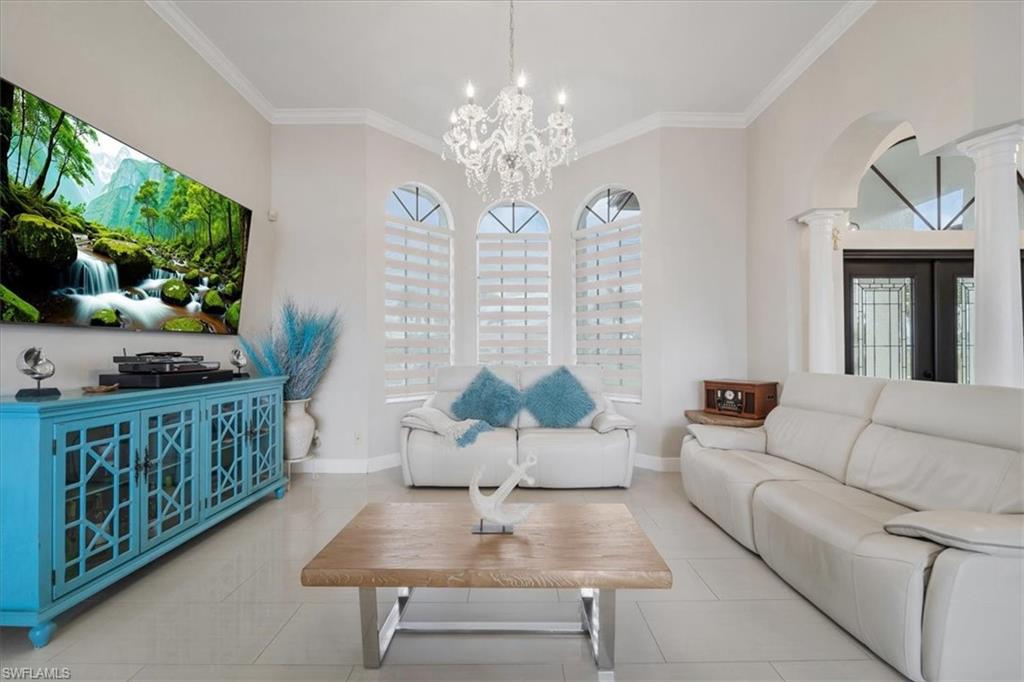 Tiled living room featuring ornamental molding, healthy amount of natural light, and a chandelier