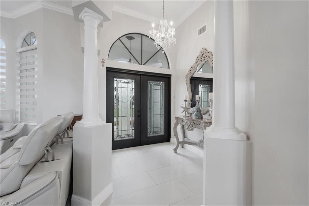 Tiled foyer entrance with decorative columns, french doors, ornamental molding, a chandelier, and a high ceiling